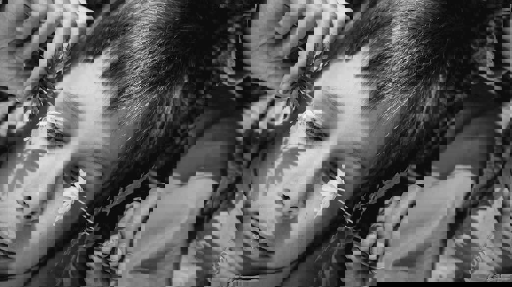 Närbild på pojke som ligger på marken och håller blommor framför sitt ansikte.