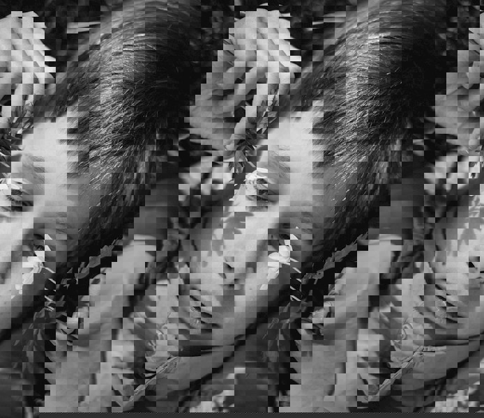 Närbild på pojke som ligger på marken och håller blommor framför sitt ansikte.